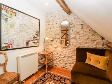 A small room with a stone wall mirror map wooden chair side table lamp and cushioned seat at Nympy Cottage in Nympsfield near Nailsworth