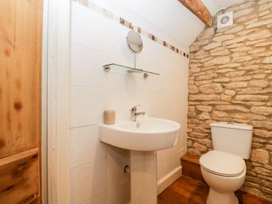 A bathroom with a pedestal sink a toilet a tiled wall with a shelf and a stone wall at Nympy Cottage in Nympsfield near Nailsworth