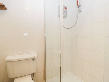 A bathroom with a toilet and a corner shower with glass door and white tiled walls at Nympy Cottage in Nympsfield near Nailsworth