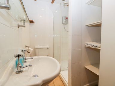 A bathroom with a sink a toilet a shower enclosure and shelves with towels at Nympy Cottage in Nympsfield near Nailsworth