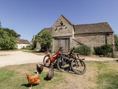 Two bicycles and four chickens on grass in front of a stone barn with wooden doors at Nympy Cottage in Nympsfield near Nailsworth