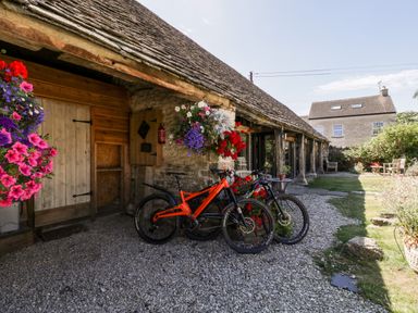 A stone cottage entrance with two bicycles and hanging flower baskets at Nympy Cottage in Nympsfield near Nailsworth