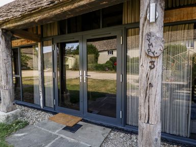 A glass double door entrance with wooden beams and stone steps at Nympy Cottage in Nympsfield near Nailsworth