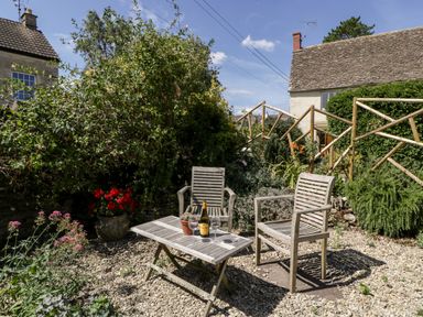 An outdoor garden area with two wooden chairs and a wooden table on gravel outside cottages at Nympy Cottage in Nympsfield near Nailsworth