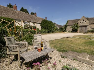 An outdoor garden area with wooden chairs and table and stone buildings in the background at Nympy Cottage in Nympsfield near Nailsworth