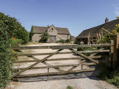 A wooden gate with a farm name sign in front of stone farm buildings and a gravel driveway at Bay Tree Farm in Nympsfield near Nailsworth