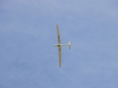 A white glider airplane flying in a clear blue sky