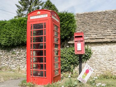 A red telephone box and a red post box next to a stone wall with greenery
