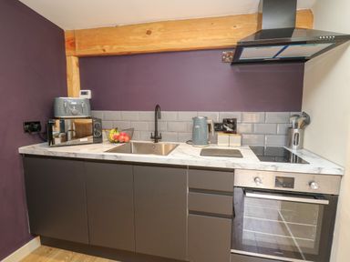 A kitchen with a sink, microwave, toaster, kettle, stovetop, oven, and utensils in containers at Daffodil in Llangadfan
