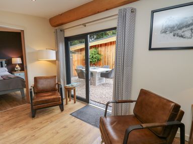 A sitting area with two brown leather chairs a small wooden side table and a sliding glass door leading to an outdoor patio at Daffodil in Llangadfan