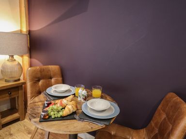 A small wooden dining table with two place settings and a breakfast platter with croissants grapes and jam in a room with brown leather chairs and a lamp on a wooden side table at Daffodil in Llangadfan