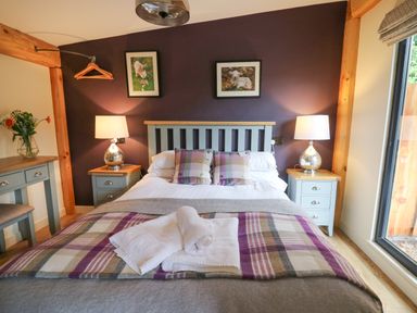 A bedroom with a double bed two bedside tables with lamps a dressing table with flowers and a window at Daffodil in Llangadfan