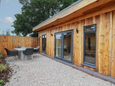 An outdoor patio area with a table and chairs next to a wooden building with glass doors and windows at Rhosyn in Llangadfan