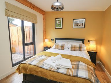 A bedroom with a bed with plaid blankets and pillows two bedside tables with lamps and a large window at Rhosyn in Llangadfan