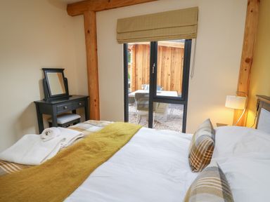 A bedroom with a bed with pillows and blankets a dressing table with a mirror a window with a blind and a view of an outdoor patio at Rhosyn in Llangadfan