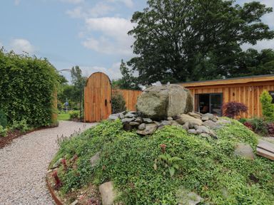 A garden path with a wooden gate a rock water feature and wooden building at Rhosyn in Llangadfan