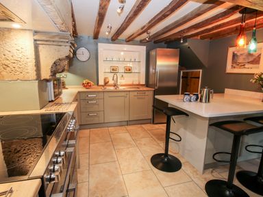 A kitchen with wooden beams on the ceiling a stove a sink a refrigerator and a breakfast bar with stools at Pentre Hall in Bronygarth near Chirk