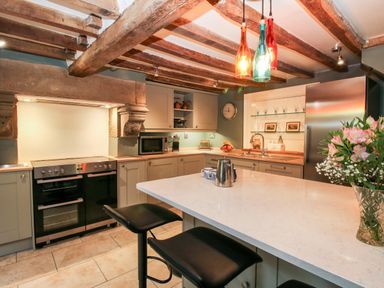 A kitchen with an island counter and bar stools under exposed wooden beams at Pentre Hall Bronygarth near Chirk