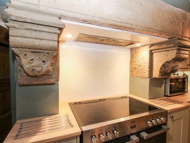 A kitchen stove with a ceramic cooktop under a stone hood with decorative corbels at Pentre Hall in Bronygarth near Chirk