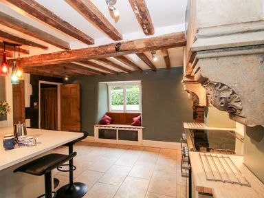 A kitchen with wooden ceiling beams a stone range cooker a window seat and a breakfast bar with stools at Pentre Hall Bronygarth near Chirk