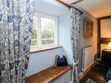 A window alcove with blue patterned curtains and a wooden seat with a blue cushion at Pentre Hall in Bronygarth near Chirk