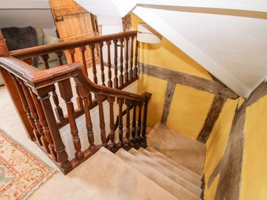 A carpeted staircase with wooden banister and yellow walls with wooden beams at Pentre Hall in Bronygarth near Chirk