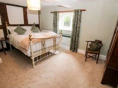 A bedroom with a metal framed bed green curtains a wooden chair and a small table at Pentre Hall in Bronygarth near Chirk