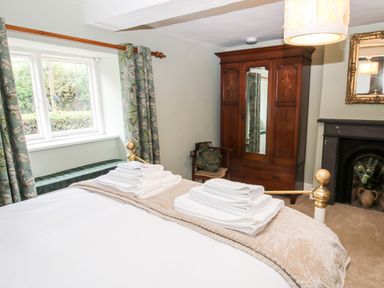 A bedroom with a bed with folded towels an antique wardrobe a chair a fireplace and a window with curtains at Pentre Hall in Bronygarth near Chirk
