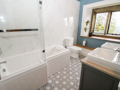 A bathroom with a bathtub shower toilet double sinks and a window with a plant on the sill at Pentre Hall in Bronygarth near Chirk
