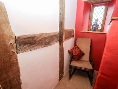 A corner with a beige rocking chair and a red cushion next to a small window with a vase on the ledge at Pentre Hall in Bronygarth near Chirk