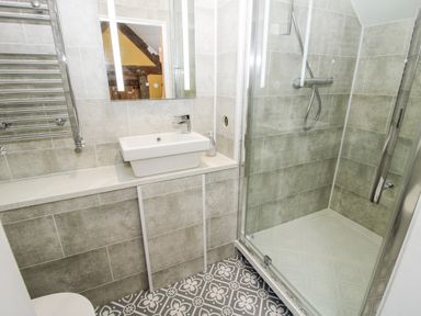 A bathroom with a sink a mirror a shower with glass doors and a patterned tile floor at Pentre Hall in Bronygarth near Chirk