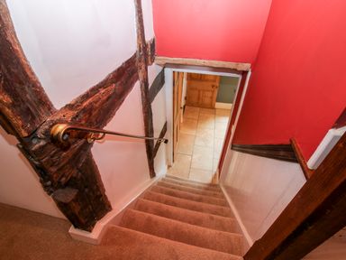 A carpeted staircase with a wooden handrail and exposed wooden beams leading down to a tiled floor with wooden doors at Pentre Hall in Bronygarth near Chirk