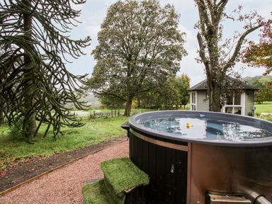 An outdoor hot tub near trees and a small garden building at Pentre Hall in Bronygarth near Chirk