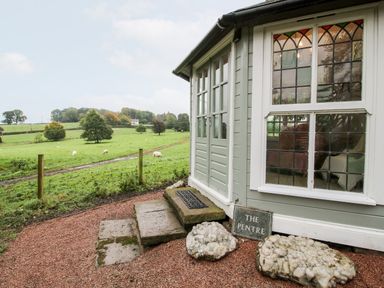Exterior of a small building with stone steps and stained glass windows beside a green field with grazing sheep at Pentre Hall Bronygarth near Chirk