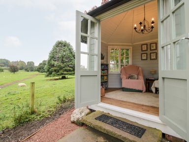 An open door leading to a small room with a chair covered with a blanket a bookshelf and framed pictures on the wall at Pentre Hall in Bronygarth near Chirk