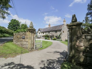 A stone house with a tiled roof behind a white gate and stone wall at Pentre Hall Bronygarth near Chirk