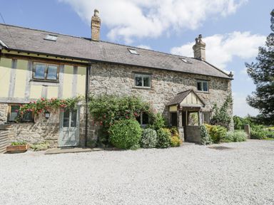 Stone and timber house with bushes and flowers in front and gravel driveway at Pentre Hall in Bronygarth near Chirk