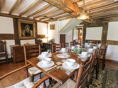 A dining room with a wooden table set for eight with bowls plates and glasses antique wooden chairs exposed beams on ceiling and walls and paintings at Pentre Hall in Bronygarth near Chirk