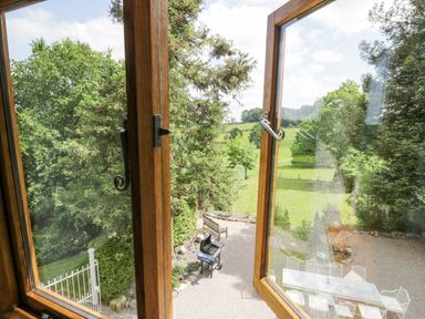 A garden with a wooden bench a barbecue grill and a white metal table with chairs viewed through an open wooden window at Pentre Hall in Bronygarth near Chirk