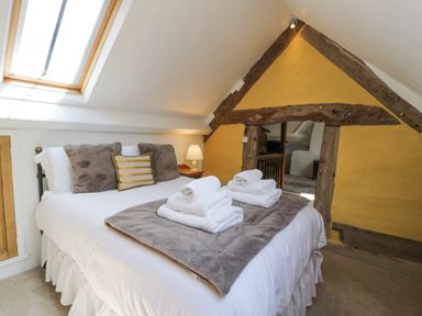 A bedroom with a bed with pillows and folded towels under a skylight with exposed wooden beams on a yellow wall at Pentre Hall in Bronygarth near Chirk