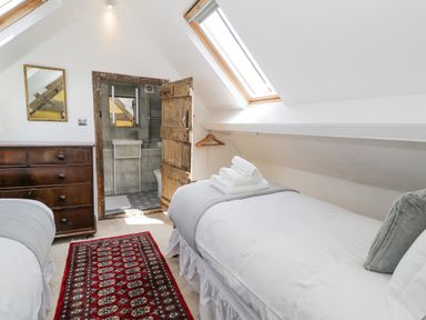 A bedroom with two single beds a wooden dresser a red patterned rug a skylight and a bathroom through an open wooden door at Pentre Hall Bronygarth near Chirk