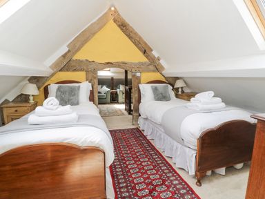 A bedroom with two single beds with white linens a red patterned rug and exposed wooden beams at Pentre Hall Bronygarth near Chirk