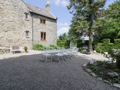 An outdoor patio area with a long table and chairs next to a stone house at Pentre Hall in Bronygarth near Chirk