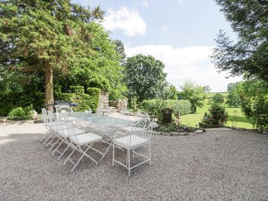 An outdoor patio area with a long table and white chairs surrounded by greenery at Pentre Hall in Bronygarth near Chirk