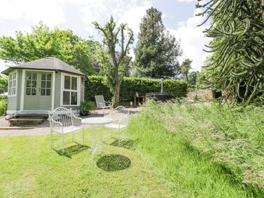 A garden with a white metal table and chairs a wooden summerhouse and trees at Pentre Hall Bronygarth near Chirk