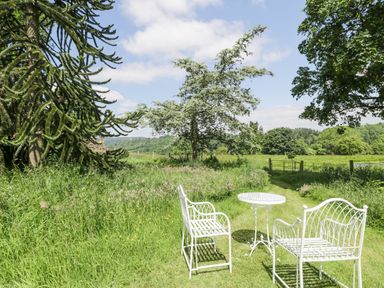 A garden area with white metal chairs and a table on grass near trees and a field at Pentre Hall in Bronygarth near Chirk