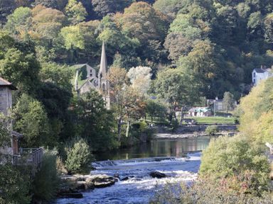 A river flowing through a village with trees hills and a church with a tall spire in the background at Pentre Hall in Bronygarth near Chirk