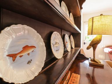 Decorative fish plates on wooden shelves and a lamp with a bird base on a wooden table at Warren Cottage in Bures near Assington