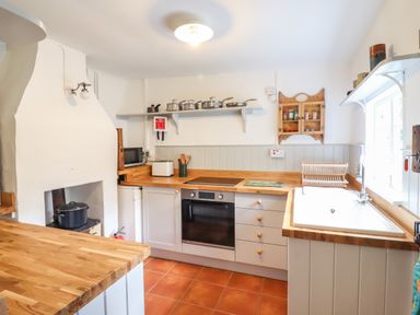 A kitchen with wooden countertops white cabinets a stove a sink and pots on a shelf at Warren Cottage in Bures near Assington
