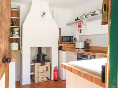 A kitchen with a wood stove fire extinguisher microwave and pots on a shelf at Warren Cottage in Bures near Assington